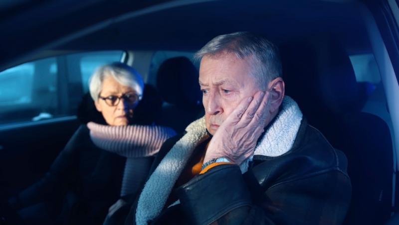 Imagine cu un bătrân îngrijorat și soția sa. Cei doi stau în mașină