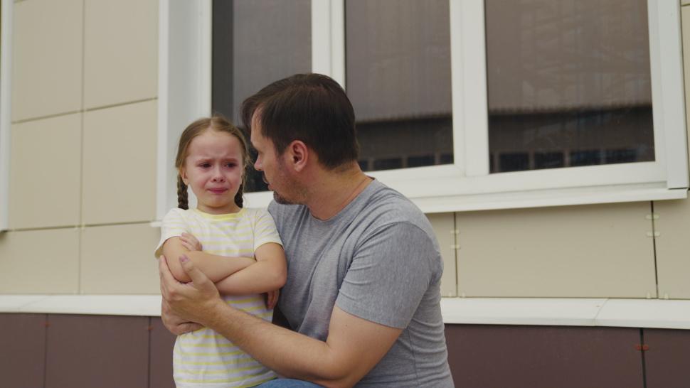 Imagine cu o fetiță supărată care plânge și tatăl ei care a certat-o