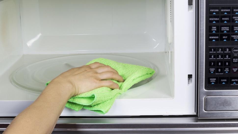 Mâna unei femei care curăță cuptorul cu microunde