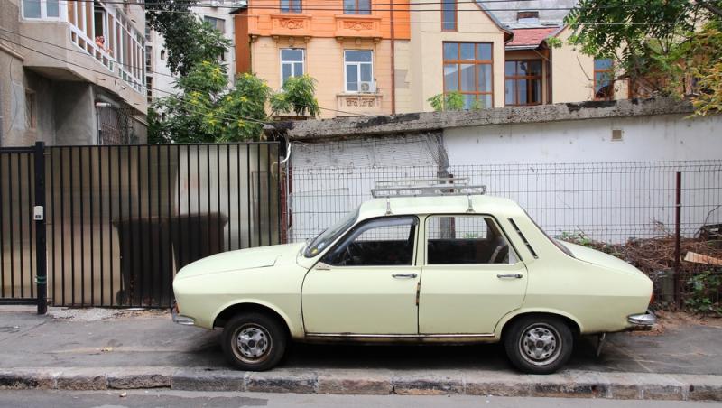 dacia 1300 crem parcată pe trotuar în fața unu gard