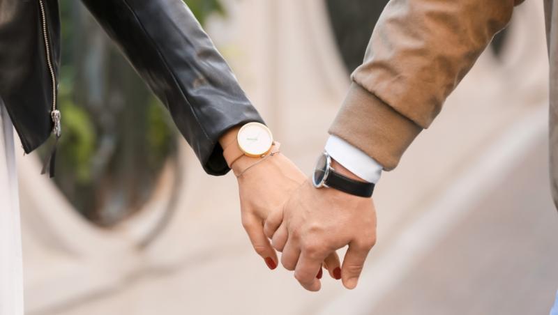 Un cuplu care se ține de mână, la mâna fiecăruia aflându-se un ceas