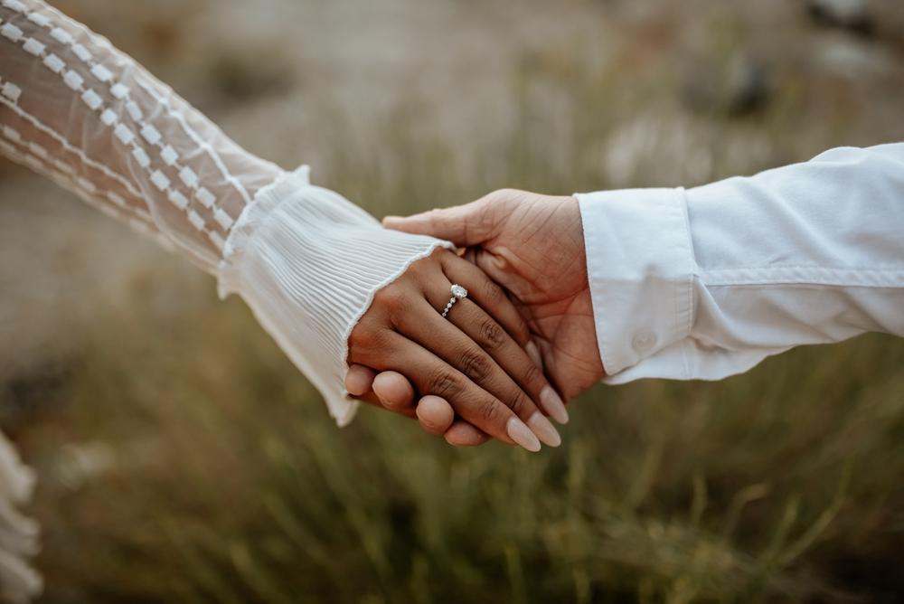 mână de femeie îmbrăcată în mireasă cu inel pe deget care ține o mână de bărbat în cămașă