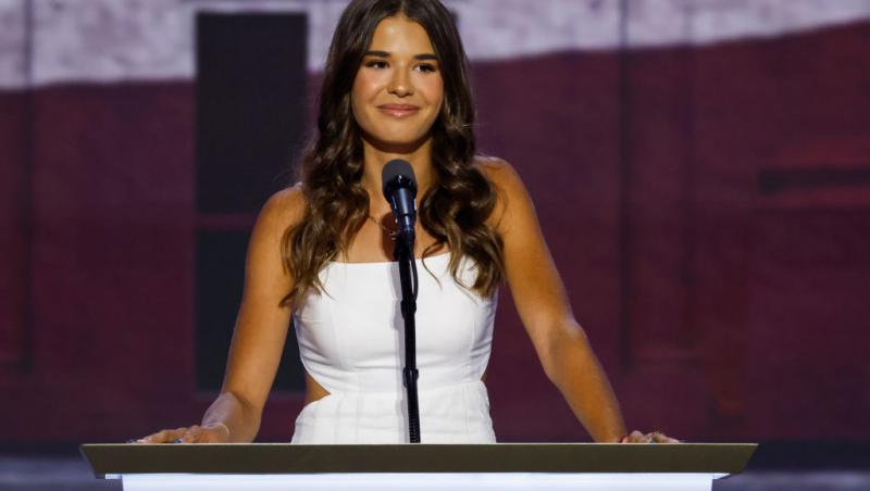 Kai Madison Trump îmbrăcată într-o rochie albă cu decupaje, la pupitru