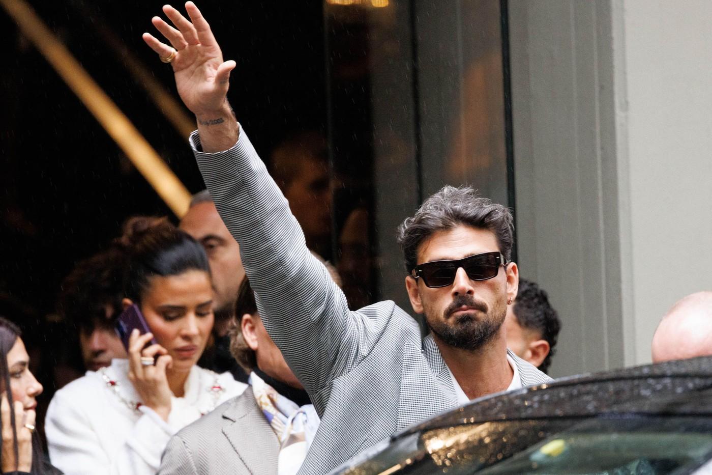 Michele Morrone îmbrăcat într-un sacou elegant cu model, cu ochelari de soare nergi, în timp ce face cu mâna