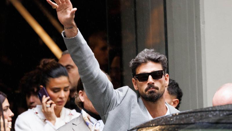 Michele Morrone îmbrăcat într-un sacou elegant cu model, cu ochelari de soare nergi, în timp ce face cu mâna