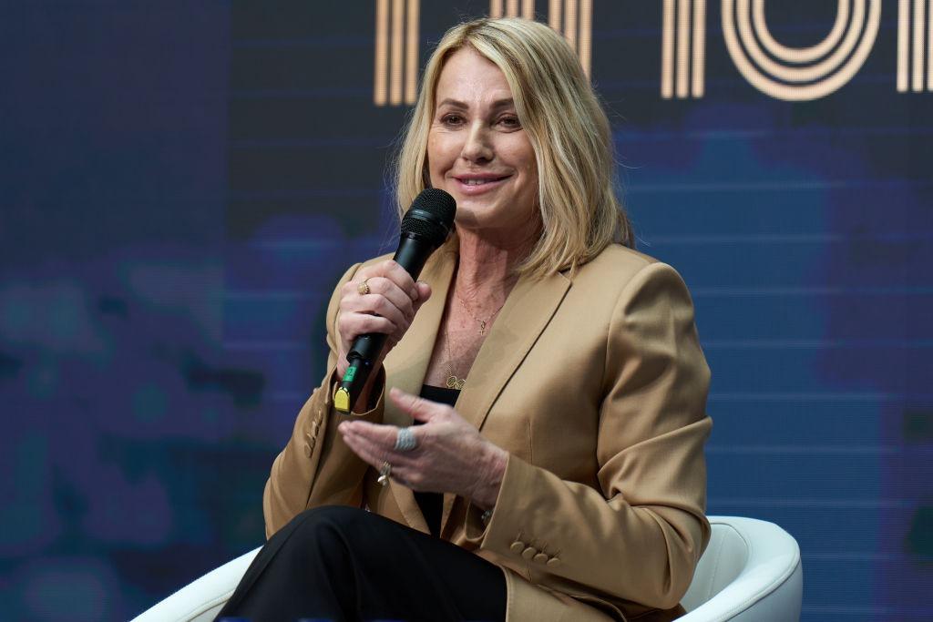 Nadia Comăneci îmbrăcată cu un sacou maro elegant, vorbind la microfon