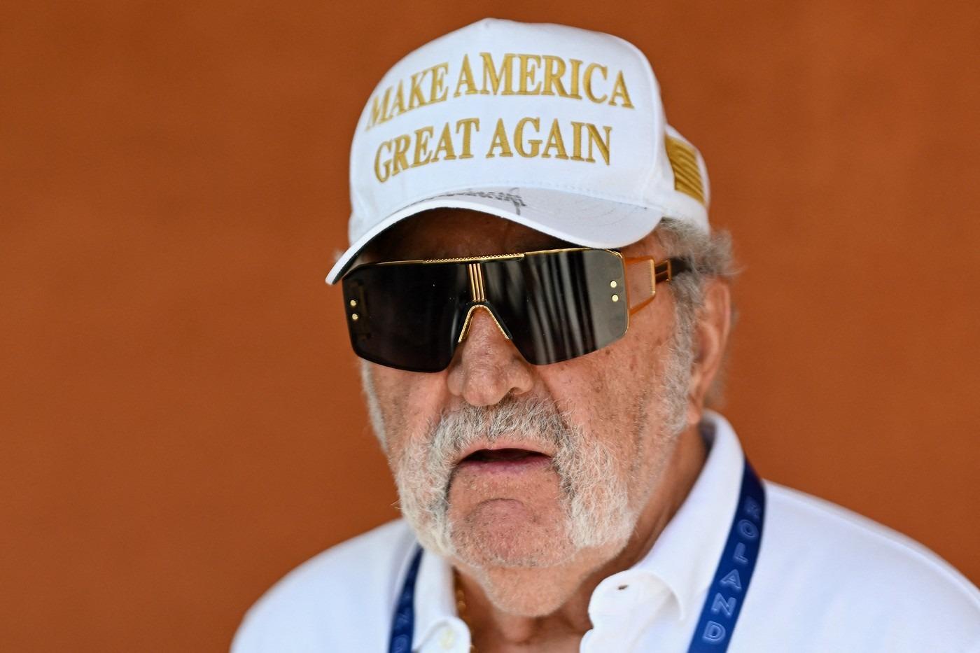 Ion Țiriac îmbrăcat cu o cămașă albă, accesorizată cu o șapcă cu ochelari de soare