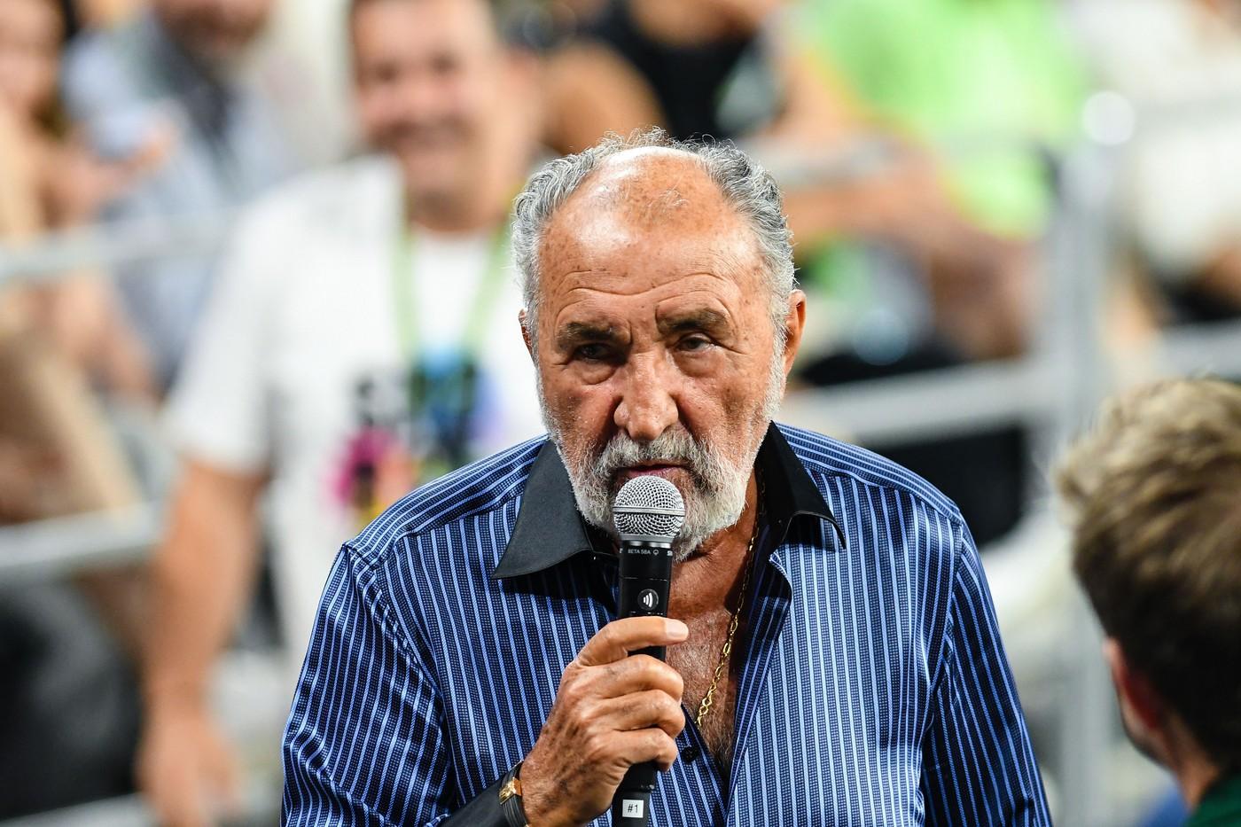 Ion Țiriac îmbrăcat cu o cămașă bleumarin, vorbind la microfon