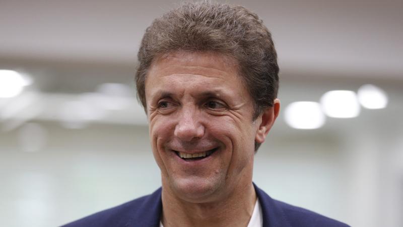 Gică Popescu &icirc;mbrăcat cu un sacou bleumarin peste un tricou alb, z&acirc;mbind