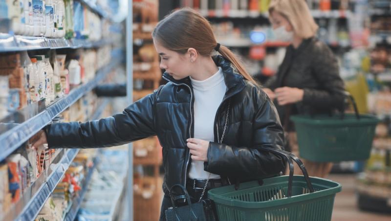 t&acirc;nără care ține un coș de cumpărături și se uită la produsele de pe raftul unui supermarket