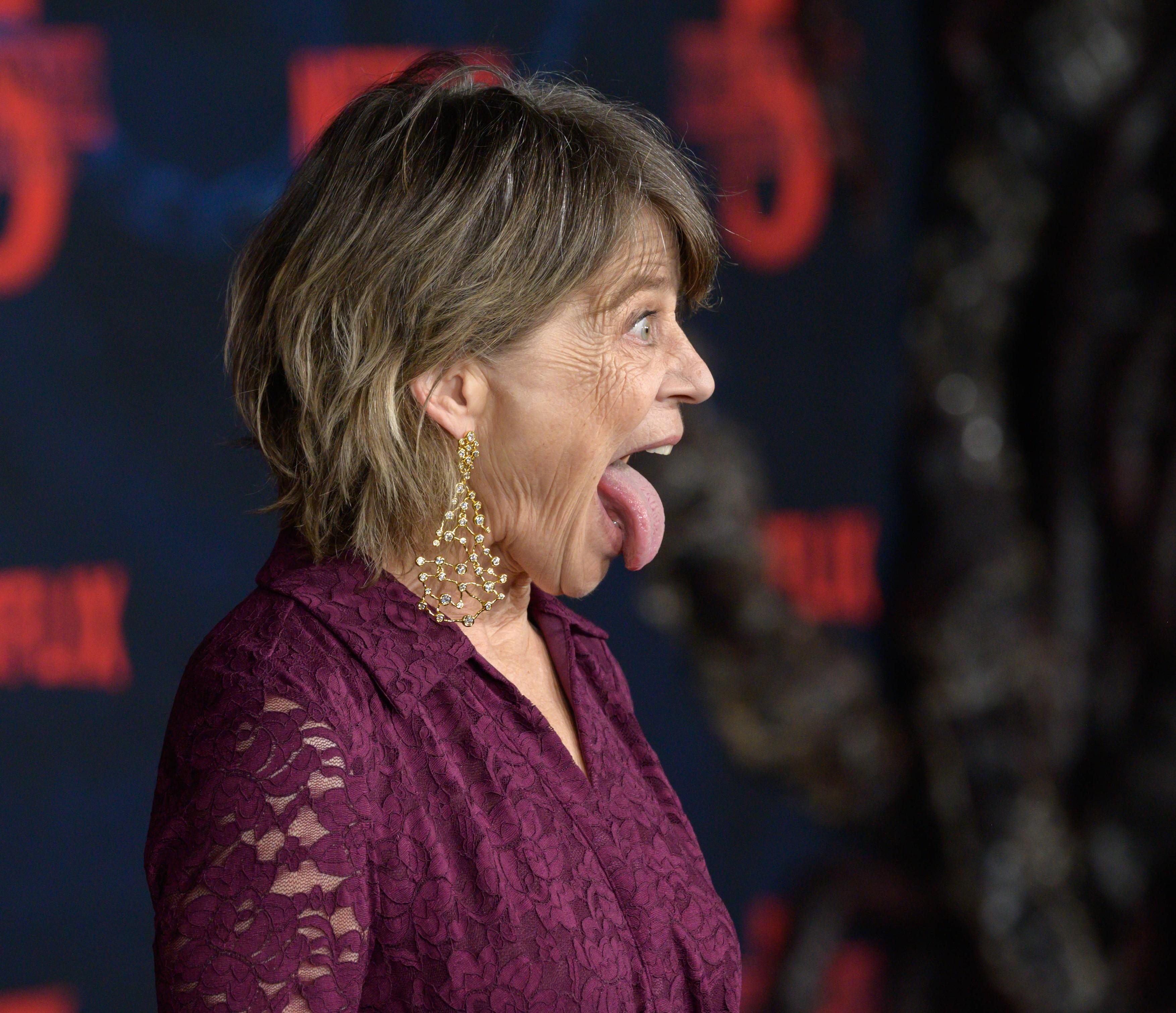 Linda Hamilton, noiembrie 2025, covorul roșu Stranger Things, îmbrăcată în mov, cu limba scoasă