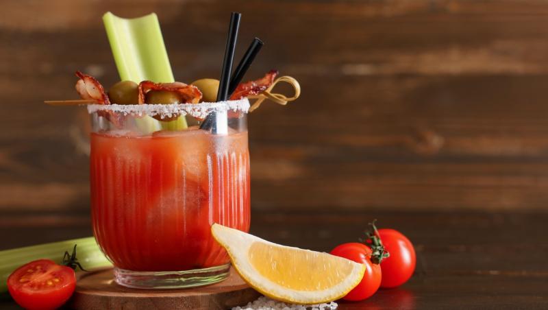 Un pahar de cocktail Bloody Mary cu bacon, măsline, lăm&acirc;ie și țelină pe fundal de lemn