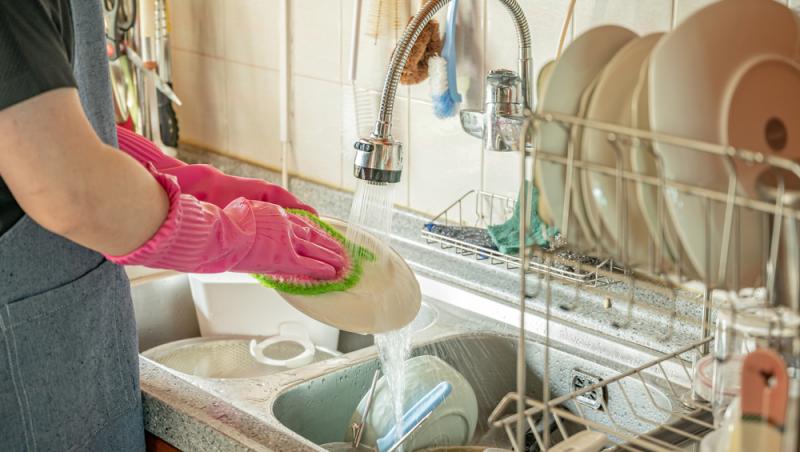 femeie cu mănuși care spală vasele în chiuvetă