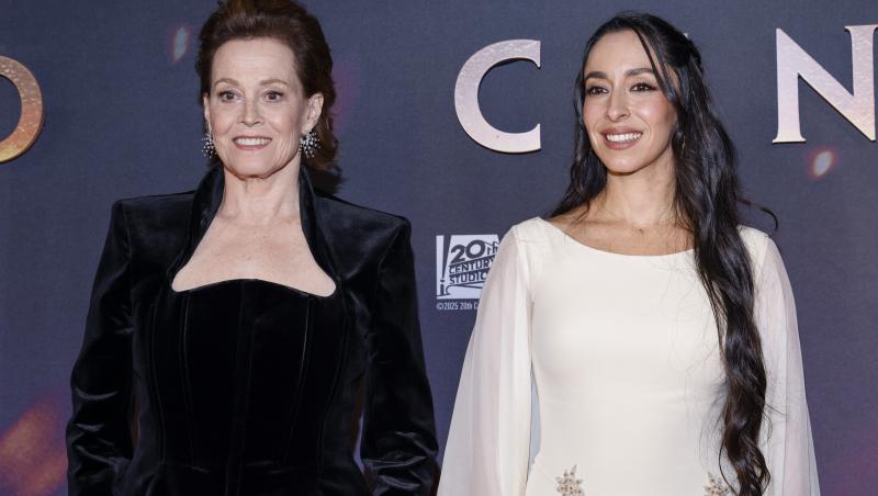 Oona Chaplin, covorul roșu Avatar, decembrie 2025, rochie albă, cu Sigourney Weaver, &icirc;mbrăcată &icirc;n negru