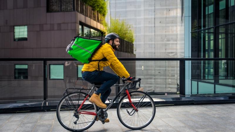 tânăr pe bicicletă cu geantă de livrator în spate