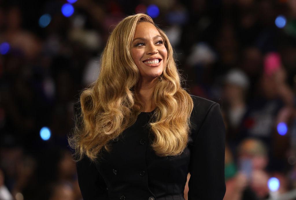 Beyoncé îmbrăcată într-o rochie neagră elegantă, cu părul blond lăsat pe spate, în bucle lejere