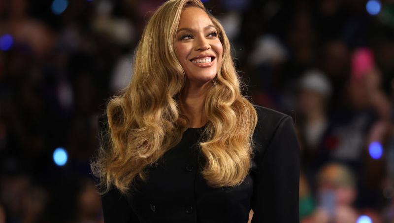 Beyoncé îmbrăcată într-o rochie neagră elegantă, cu părul blond lăsat pe spate, în bucle lejere