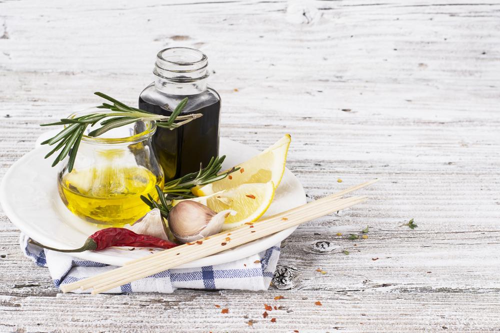 sticlă de oțet balsamic, sticlă cu ulei de măsline, lămâie și crenguță de rozmarin pe o tavă