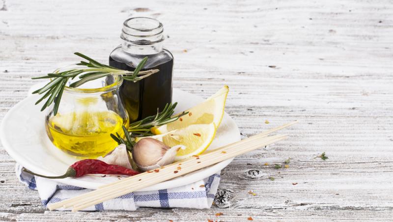 sticlă de oțet balsamic, sticlă cu ulei de măsline, lămâie și crenguță de rozmarin pe o tavă