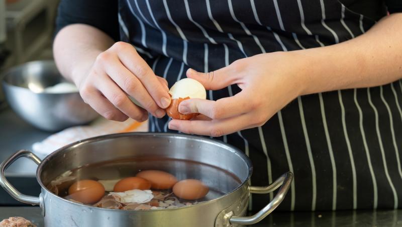 imagine cu mainile unei femei care curata un ou fiert deasupra unei oale cu apa si alte oua