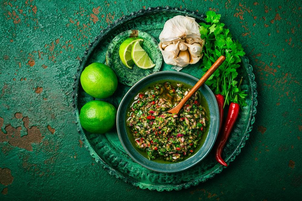 sos chimmichuri într-un bol cu limetă, usturoii, ardei iute și ierburi alături