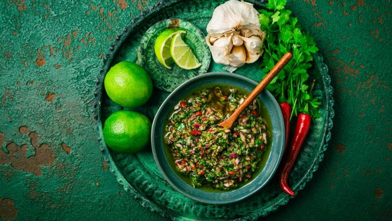 sos chimmichuri într-un bol cu limetă, usturoii, ardei iute și ierburi alături