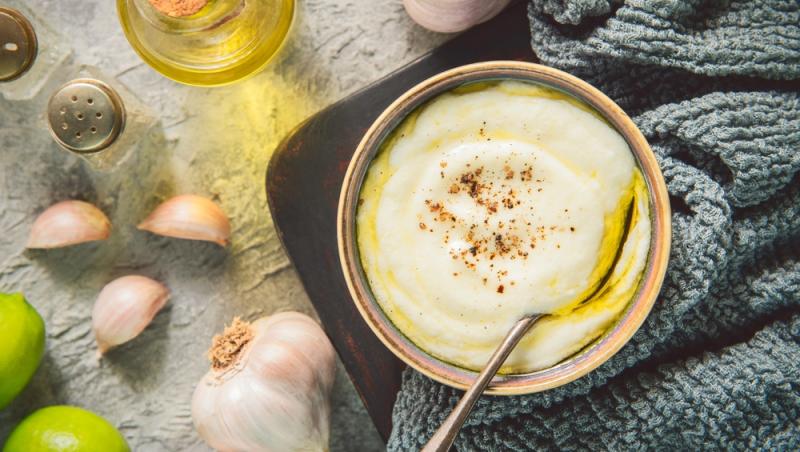 sos toum înt-un bol cu linguriță, cu căței de usturoi, limetă și ulei alături