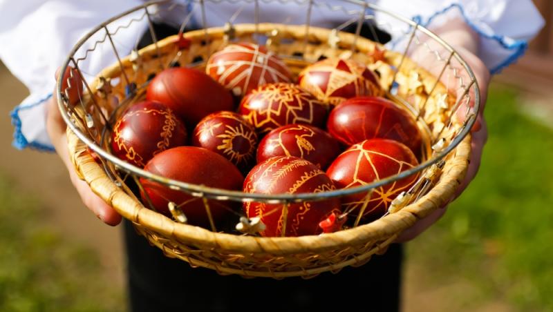 imagine cu o femeie care tine in maini un cos de paie cu ouă rosii traditionale de paste