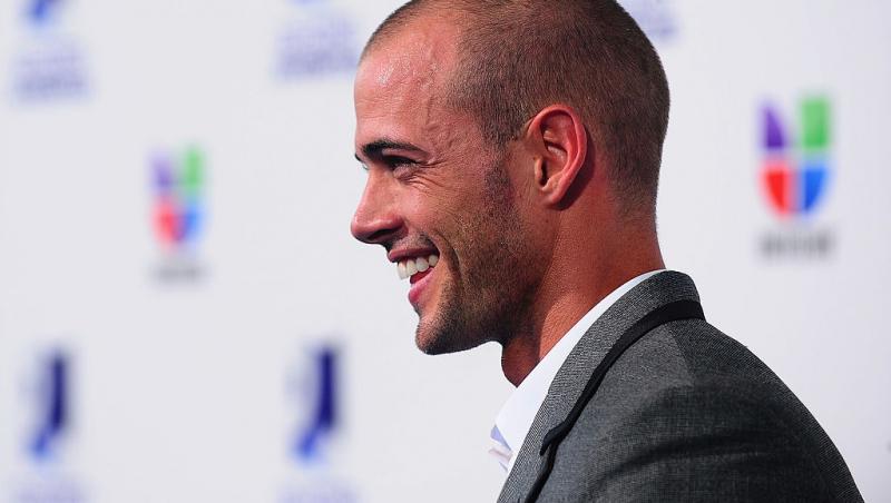 William Levy îmbrăcat cu un costum gri, zâmbind fericit