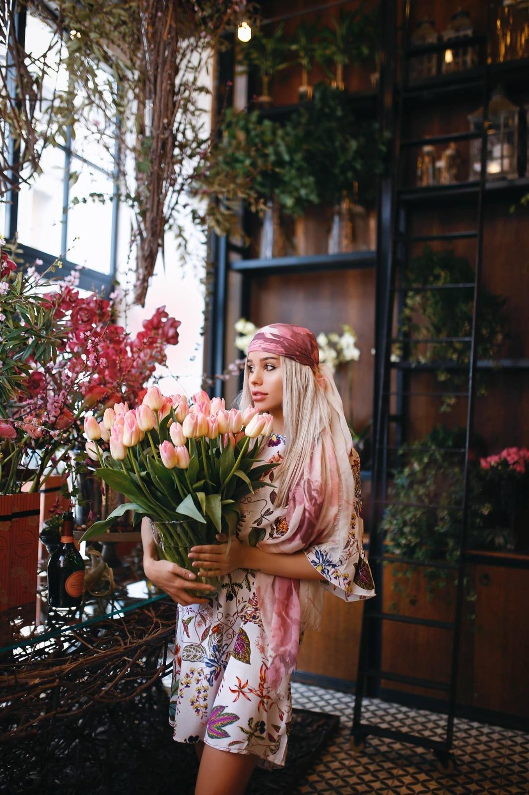 Carmen Grebenișan îmbrăcată cu o rochie colorată, ținând un buchet de lalele în mâini