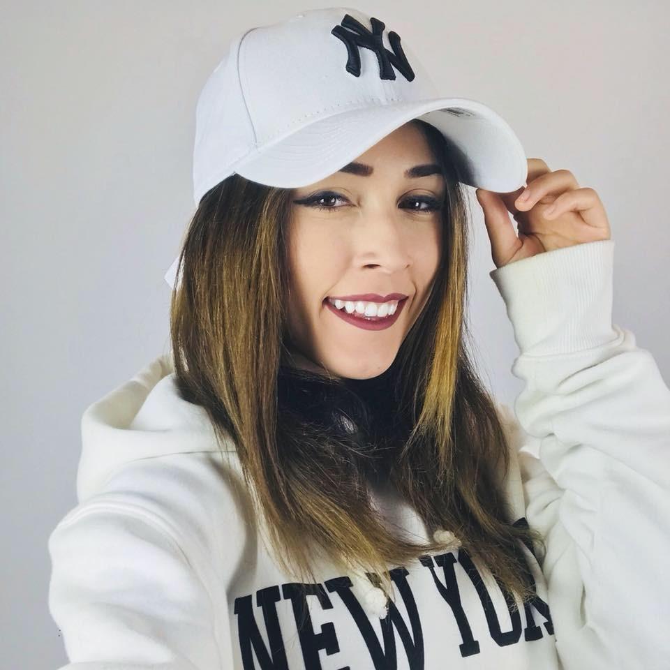 Andra Gogan îmbrăcată cu un hanorac alb și o șapcă asortată