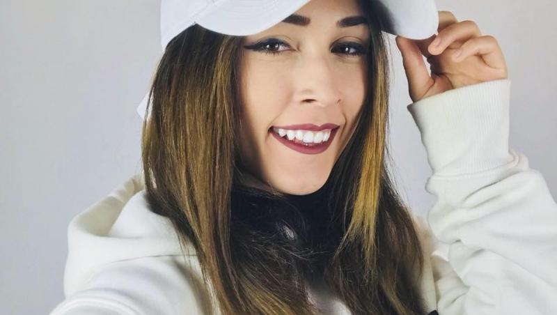Andra Gogan îmbrăcată cu un hanorac alb și o șapcă asortată