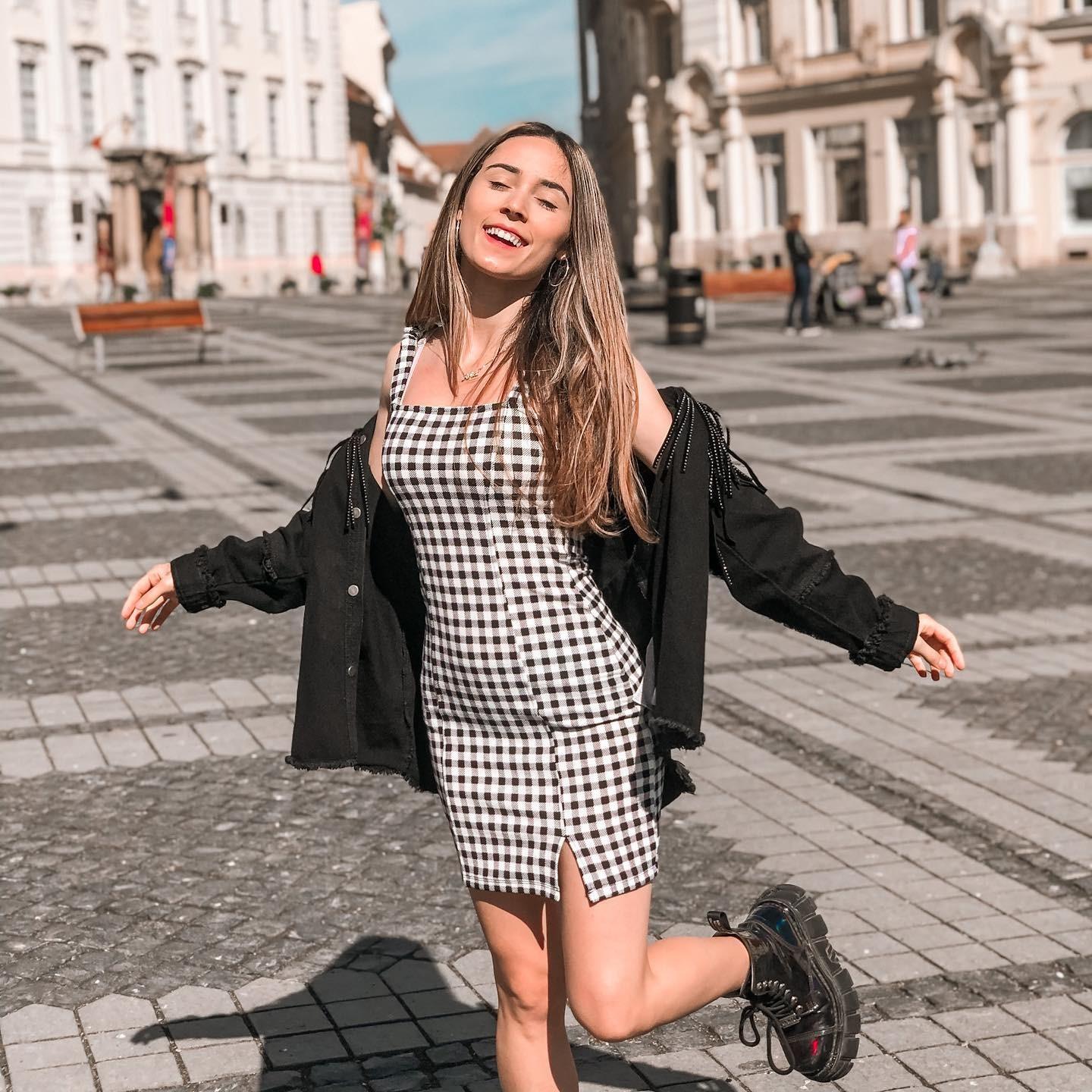 Andra Gogan îmbrăcată cu o rochie în carouri și un hanorac negru