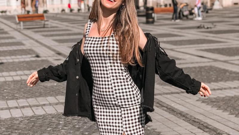 Andra Gogan îmbrăcată cu o rochie în carouri și un hanorac negru