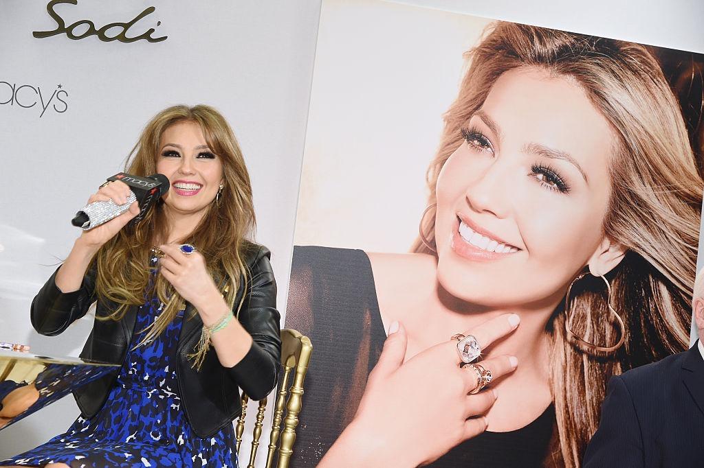 Thalía Sodi îmbrăcată cu o rochie bleumarin, sub o jachetă neagră din piele, zâmbind fericită