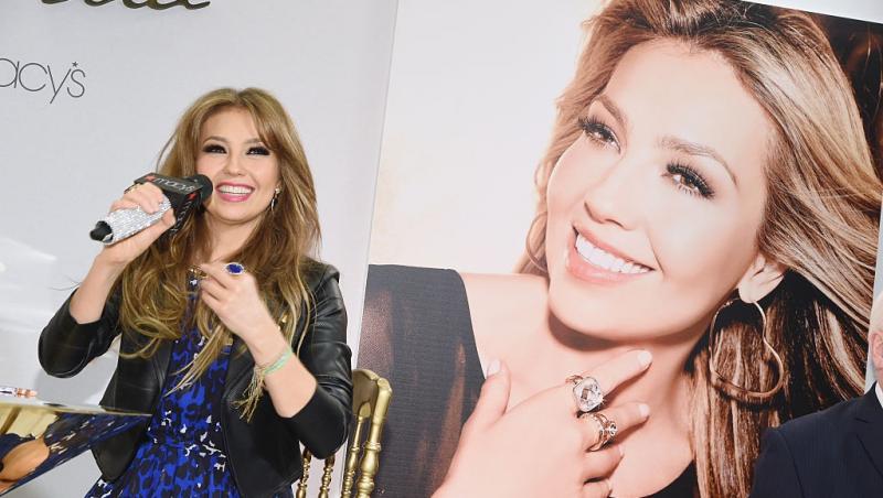 Thalía Sodi îmbrăcată cu o rochie bleumarin, sub o jachetă neagră din piele, zâmbind fericită