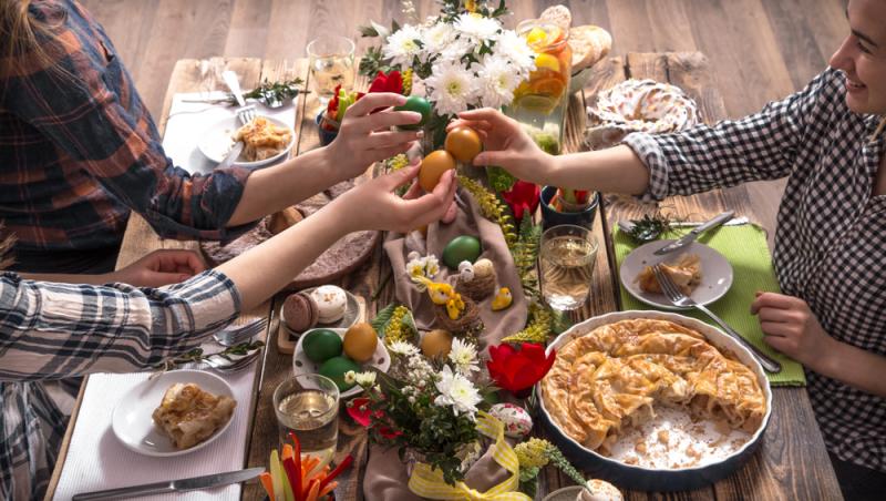 persoane tinere în jurul mesei pline ciocnind ouă colorate