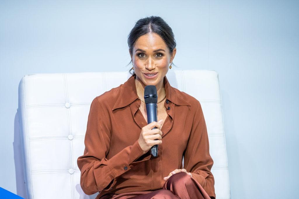 Meghan Markle îmbrăcată într-o cămașă cărămizie, vorbind la microfon
