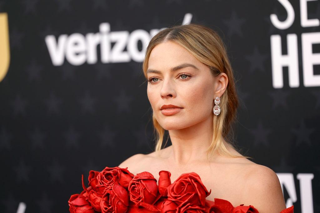 Margot Robbie îmbrăcată cu o rochie roșie elegantă, fără mâneci, împodobită cu trandafiri