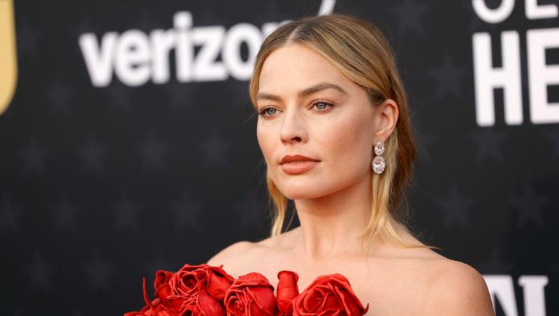 Margot Robbie îmbrăcată cu o rochie roșie elegantă, fără mâneci, împodobită cu trandafiri
