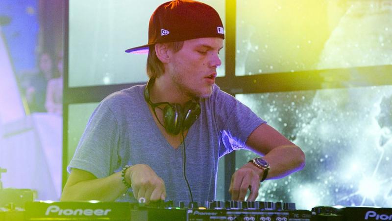 Avicii îmbrăcat cu un tricou gri, mixând muzică pe scenă