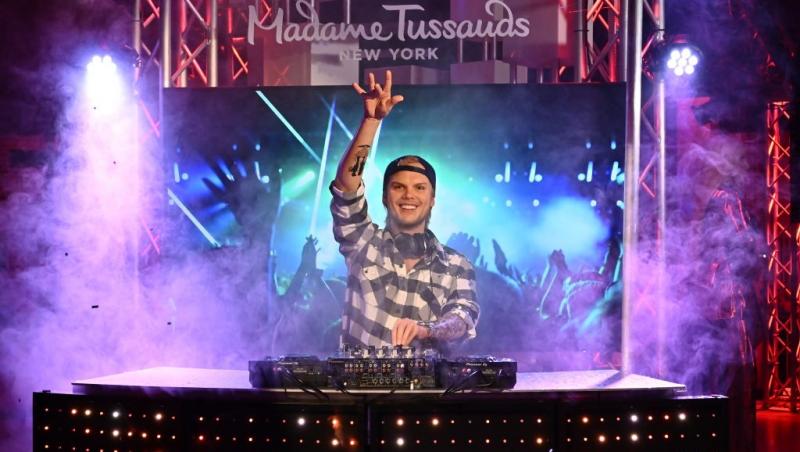 Avicii îmbrăcat cu o cămașă în carouri, mixând muzică pe scenă