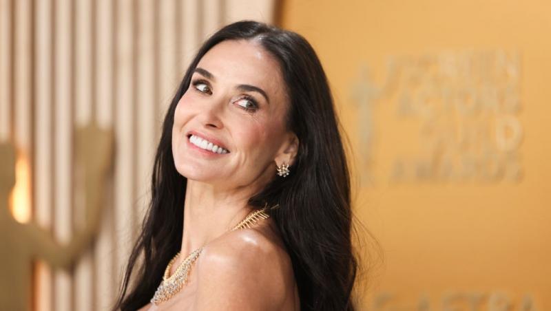 Demi Moore îmbrăcată într-o rochie neagră mulată, fără mâneci, zâmbind fericită