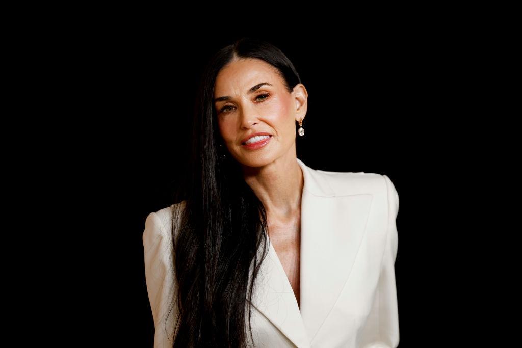 Demi Moore îmbrăcată într-o un sacou alb elegant, cu părul negru, lung, lasat pe spate