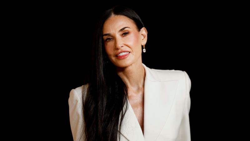 Demi Moore îmbrăcată într-o un sacou alb elegant, cu părul negru, lung, lasat pe spate