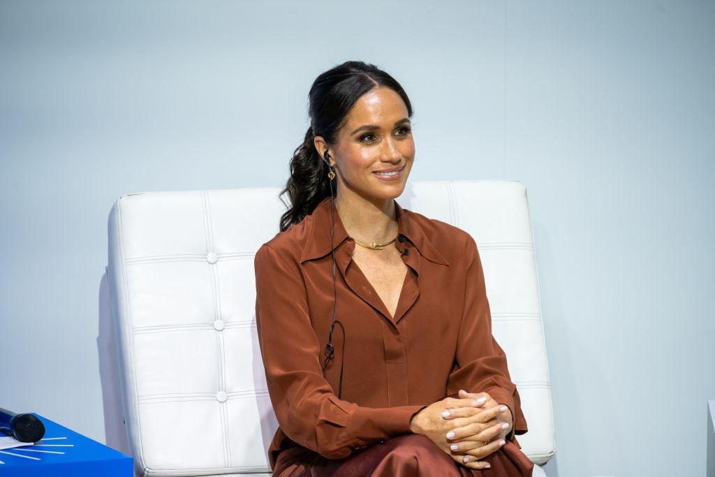 Meghan Markle îmbrăcată într-o cămașă cărămizie, zâmbind