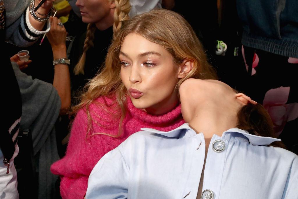 Bella Hadid, îmbrăcată cu o cămașă bleumarin, alături de sora ei, Gigi Hadid, îmbrăcată cu un pulover roz