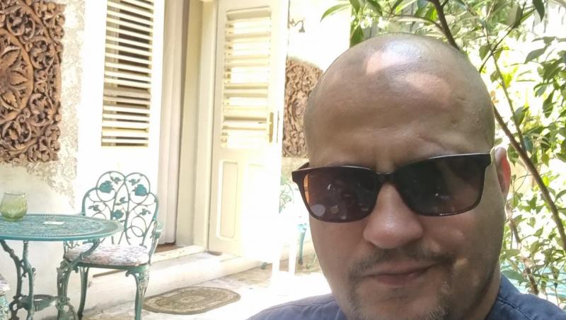 Șerban Huidu îmbrăcat cu un tricou din denim, purtând ochelari de soare