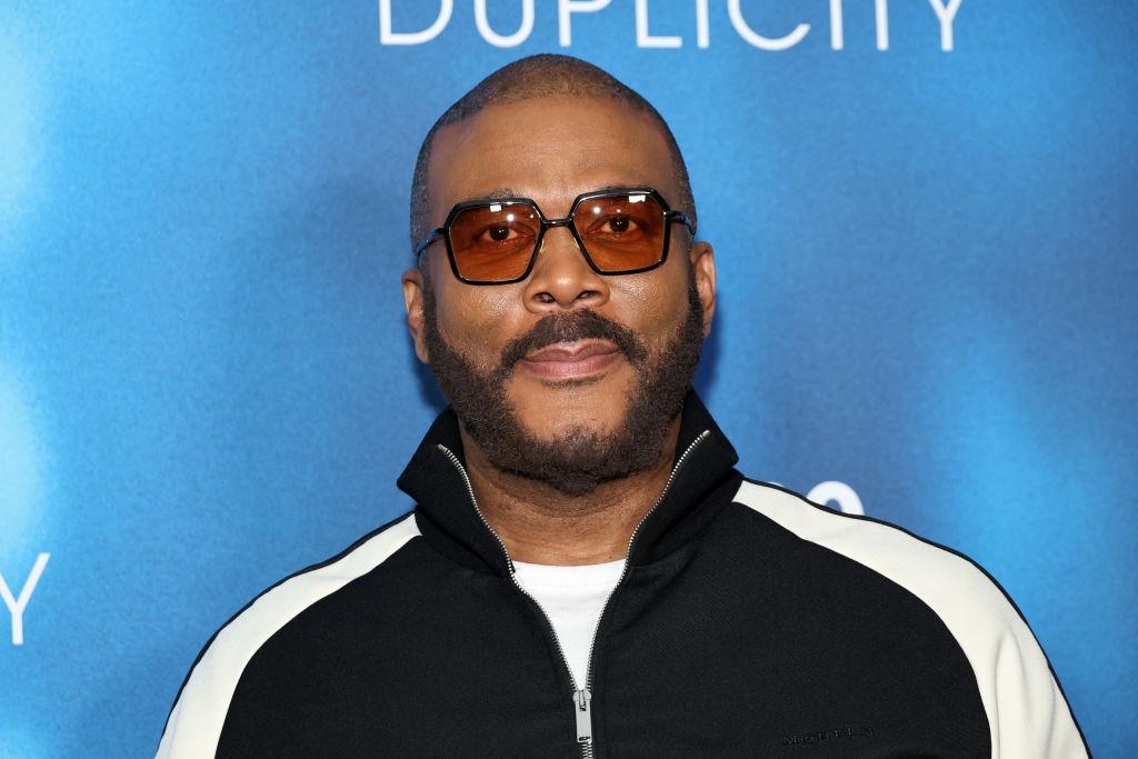 Tyler Perry îmbrăcat cu o bluză neagră cu dungi albe, accesoriztă cu ochelari de soare