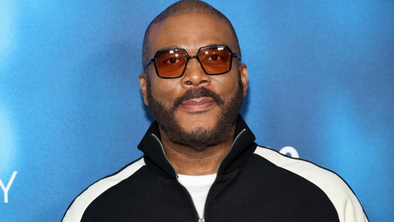 Tyler Perry îmbrăcat cu o bluză neagră cu dungi albe, accesoriztă cu ochelari de soare